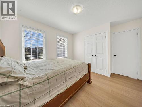 Room featuring wood-finish flooring, two windows with white blinds, a bi-fold closet door with black hardware, and a single-panel door with a black handle - 39 Baintree Way, Cambridge, ON - Indoor Photo Showing Bedroom
