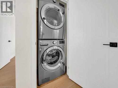 Dedicated laundry closet featuring a stacked washer and dryer, white paneled doors, black hardware, and wood-finish flooring - 39 Baintree Way, Cambridge, ON - Indoor Photo Showing Laundry Room