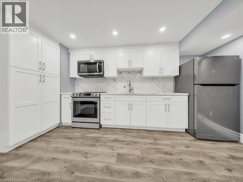 Modern kitchen featuring white shaker cabinetry, stainless steel appliances, light countertops, a marble-patterned backsplash, and wood-finish flooring - 39 Baintree Way, Cambridge, ON - Indoor Photo Showing Kitchen