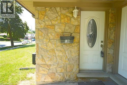 Stone veneer facade with a white entry door featuring an oval decorative glass insert, complemented by an exterior wall sconce - 136 Jansen Avenue, Kitchener, ON - Outdoor