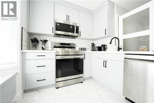 Modern kitchen featuring white cabinetry with matte black hardware, stainless steel appliances, white subway tile backsplash, white countertops, and large format tile flooring - 136 Jansen Avenue, Kitchener, ON - Indoor Photo Showing Kitchen