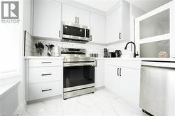 Modern kitchen featuring white cabinetry with matte black hardware, stainless steel appliances, white subway tile backsplash, white countertops, and large format tile flooring - 