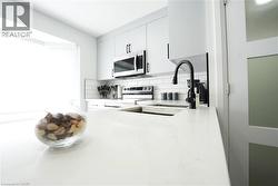 Sleek kitchen featuring expansive white countertops, a deep undermount sink with a matte black faucet, and white subway tile backsplash - 