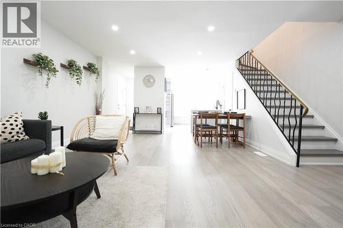 Open-concept living area featuring light wood-finish flooring, recessed lighting, a modern staircase with a black wrought iron railing and brass handrail, and a dining area with built-in countertop se - 136 Jansen Avenue, Kitchener, ON - Indoor Photo Showing Living Room
