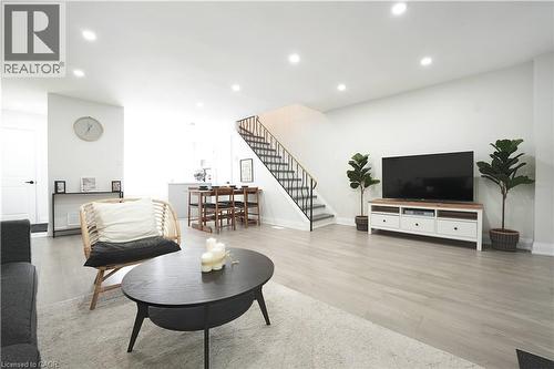Open-concept living area featuring light wood-finish flooring, recessed lighting, white walls, a dining area, and a staircase with a black metal railing - 136 Jansen Avenue, Kitchener, ON - Indoor Photo Showing Living Room