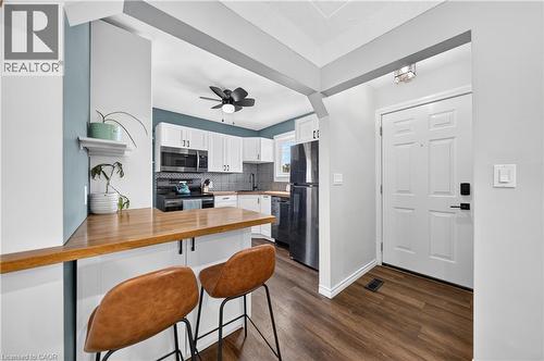 Updated kitchen featuring white shaker cabinetry, stainless steel appliances, a wood-finish peninsula countertop, and a contrasting teal accent wall - 621 Tate Avenue, Hamilton, ON - Indoor Photo Showing Kitchen