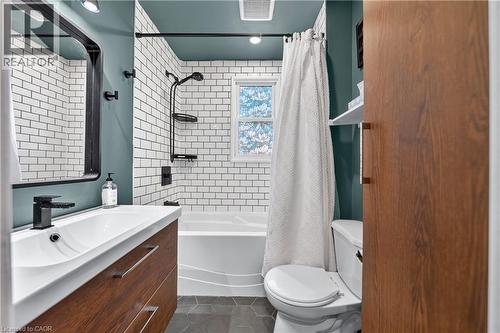 Bathroom featuring a wood-finish vanity with an integrated sink and matte black faucet, subway tile shower surround, and hexagonal floor tiles - 621 Tate Avenue, Hamilton, ON - Indoor Photo Showing Bathroom