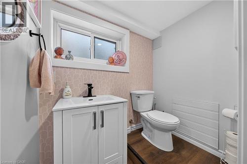 Powder room featuring a white single-sink vanity with matte black faucet, a sliding window with frosted glass, wood-finish flooring, and a white toilet - 621 Tate Avenue, Hamilton, ON - Indoor Photo Showing Bathroom