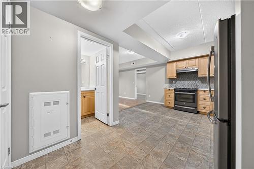 Kitchen area featuring tile flooring, light wood cabinetry, stone-finish countertops, and a full-size black range with a stainless steel hood - 155 Water Street S Unit# 203, Cambridge, ON - Indoor Photo Showing Other Room