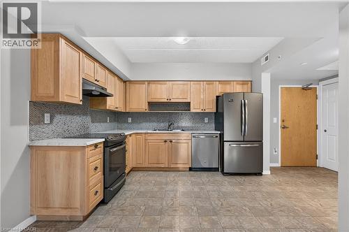 Kitchen featuring wood-finish cabinetry, stainless steel appliances, mosaic tile backsplash, white countertops, and durable tile flooring - 155 Water Street S Unit# 203, Cambridge, ON - Indoor Photo Showing Kitchen With Stainless Steel Kitchen