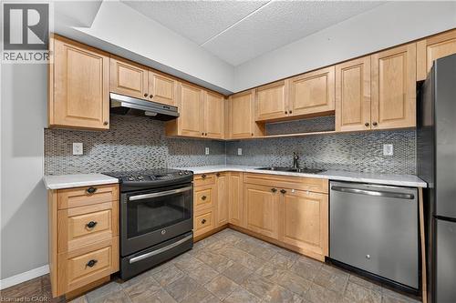 U-shaped kitchen with light wood-finish cabinetry, white countertops, and a mosaic tile backsplash - 155 Water Street S Unit# 203, Cambridge, ON - Indoor Photo Showing Kitchen With Stainless Steel Kitchen With Double Sink