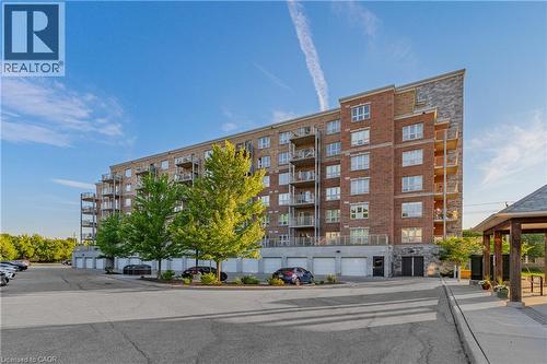 Multi-story residential building featuring brick and stone cladding, private balconies, and a ground-level parking garage - 155 Water Street S Unit# 203, Cambridge, ON - Outdoor With Facade