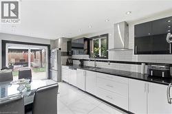 Modern kitchen featuring white subway tile backsplash with accent banding, stainless steel appliances, black countertops, and white flooring - 