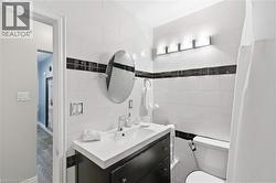 Bathroom featuring white horizontal wall tile with a black accent band, a dark wood-finish vanity with an integrated sink, an oval mirror, and a three-light vanity fixture - 