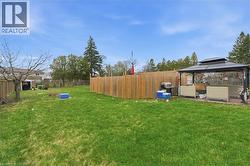 Expansive backyard featuring a manicured lawn, full privacy fencing, and a built-in gazebo with a paved patio - 