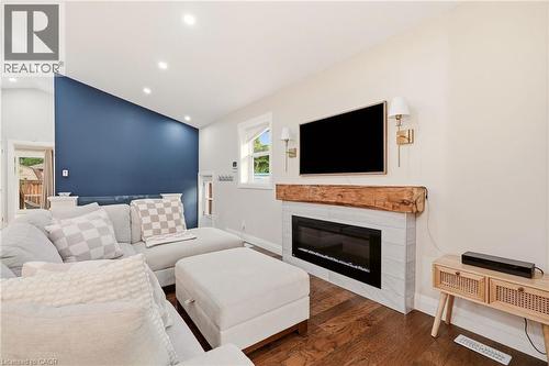 Living area with wood-finish flooring, a contemporary electric fireplace featuring a tile surround and a rustic wood mantel, and integrated wall sconces - 715 Drury Lane, Burlington, ON - Indoor Photo Showing Living Room With Fireplace