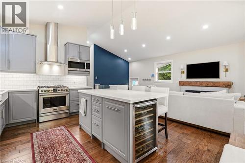 Open-concept kitchen featuring gray cabinetry, stainless steel appliances, a center island with a built-in wine refrigerator, white countertops, and wood-finish flooring - 715 Drury Lane, Burlington, ON - Indoor Photo Showing Kitchen With Upgraded Kitchen