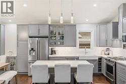 Kitchen featuring an island with seating, stainless steel appliances, a white farmhouse sink, grey cabinetry, and a subway tile backsplash - 