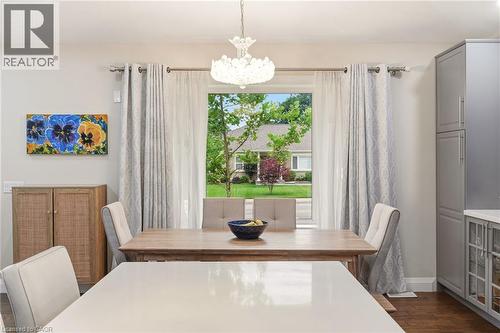 Dining area featuring a central window, wood-finish flooring, a contemporary chandelier, built-in cabinetry with glass-front uppers, and a light-toned countertop - 715 Drury Lane, Burlington, ON - Indoor Photo Showing Dining Room