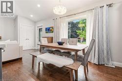 Dining area featuring wood-finish flooring, a contemporary chandelier, recessed lighting, and a large window with opaque and patterned drapery - 