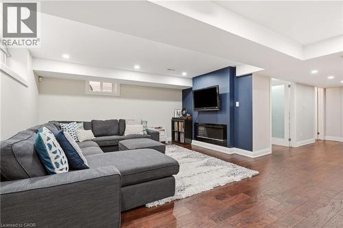 Finished lower level featuring recessed lighting, rich wood-finish flooring, a wall-mounted flat-screen television, a linear electric fireplace, and a partial glass-paneled door - 715 Drury Lane, Burlington, ON - Indoor With Fireplace