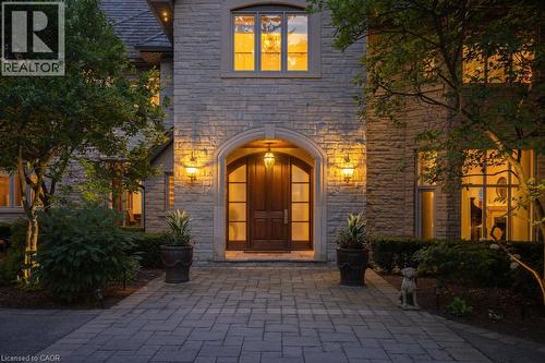 Stone facade residence featuring a grand arched entry with a solid wood door, multiple windows, and exterior sconce lighting - 4038 Lakeshore Road, Burlington, ON - Outdoor
