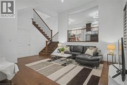 Open-concept living space featuring wood-finish flooring, a contemporary staircase with dark wood treads and metal balusters, and a half-wall overlooking an upper level - 