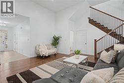 Living area featuring high ceilings, wood-finish flooring, a modern staircase with dark wood treads and metal balusters, and a white interior door - 