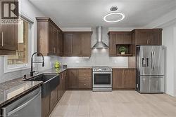 Modern kitchen featuring wood cabinetry, dark granite countertops, and stainless steel appliances - 