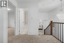 Upper-level hallway featuring plush carpet flooring, a tiered crystal chandelier, and a wood and wrought iron staircase railing - 