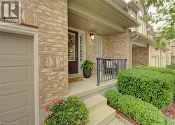 Front entry featuring light-toned brickwork, a covered porch with a black metal railing, and a dark brown entry door with sidelights - 