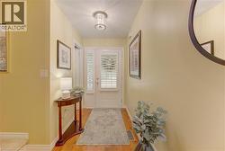 Entryway featuring wood-finish flooring, a decorative area rug, and a front door with white louvered shutters and sidelight - 