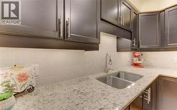 Kitchen featuring dark wood cabinetry, light-colored speckled countertops, a stainless steel double basin sink, and a tiled backsplash - 