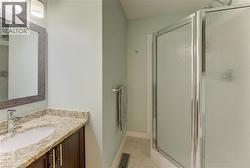 Bathroom featuring a freestanding shower with frosted glass enclosure, a single vanity with a granite-style countertop, an undermount sink, and a framed mirror - 