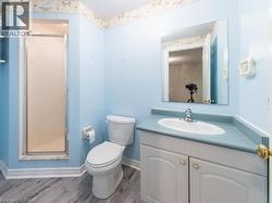 Bathroom featuring a stand-up shower with a glass door, a single vanity with an integrated sink and light blue countertop, a two-piece toilet, and wood-finish flooring - 