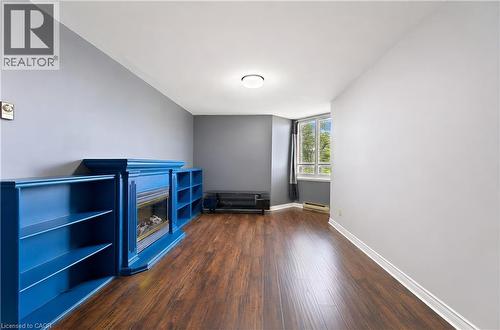 Spacious room featuring wood-finish flooring, a built-in electric fireplace with a blue mantel, integrated shelving, and a large window - 688 Preston Parkway Unit# 401, Cambridge, ON - Indoor Photo Showing Other Room