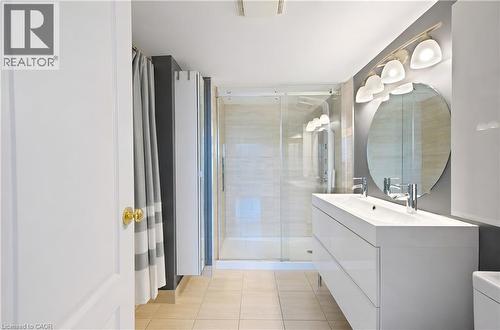 Contemporary bathroom featuring a dual vanity, integrated sinks, circular mirror, and a glass-enclosed shower - 688 Preston Parkway Unit# 401, Cambridge, ON - Indoor Photo Showing Bathroom