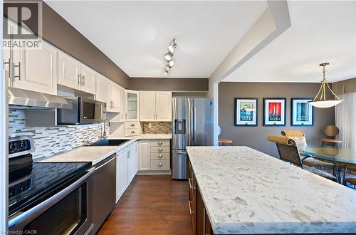 Open-concept kitchen featuring an island with a light-toned countertop, wood-finish flooring, white cabinetry, stainless steel appliances, and a tiled backsplash - 688 Preston Parkway Unit# 401, Cambridge, ON - Indoor Photo Showing Kitchen With Upgraded Kitchen