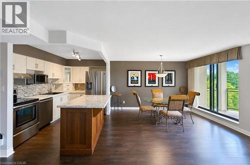 Open-concept living space featuring wood-finish flooring, a kitchen island with stone countertop, stainless steel appliances, a tile backsplash, and a sliding glass door opening to a balcony - 688 Preston Parkway Unit# 401, Cambridge, ON - Indoor Photo Showing Kitchen With Upgraded Kitchen
