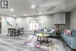 Open-concept living area featuring wood-finish flooring, recessed lighting, a sliding window with white trim, and a built-in louvered cabinet - 