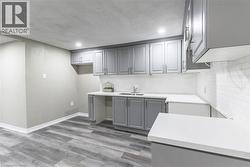 Contemporary kitchen featuring grey shaker-style cabinetry, white subway tile backsplash, and light-toned countertops - 