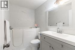 Bathroom featuring a walk-in tub, white tiled walls with subtle veining, a vanity with a light gray base and white countertop, an integrated sink with a chrome faucet, and a large framed mirror - 