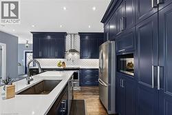 Contemporary kitchen featuring dark blue shaker cabinetry, stainless steel appliances, a white subway tile backsplash, white countertops, and wood-finish flooring - 