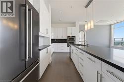 Contemporary kitchen featuring a stainless steel refrigerator, white cabinetry with silver hardware, dark countertops, a built-in oven, and a large island with an integrated sink - 