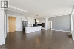 Spacious open-concept interior featuring wood-finish flooring, a contemporary kitchen island with pendant lighting, white cabinetry, integrated stainless steel appliances, and a dedicated wall space f - 