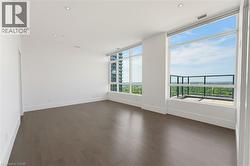 Expansive room featuring floor-to-ceiling windows, wood-finish flooring, recessed lighting, white baseboards, and a glass-paneled balcony - 