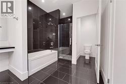 Bathroom featuring dark tiled flooring and shower surround, a white built-in bathtub, and a glass-enclosed shower with multiple shower heads - 