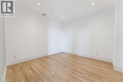 Spacious room featuring light wood-finish flooring, crisp white walls, recessed ceiling lighting, and clean white baseboards - 