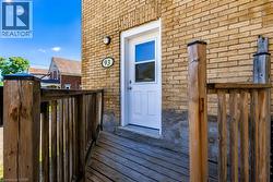 Solid brick exterior featuring a white entry door, exterior sconce lighting, and a wood-finish deck with railing - 