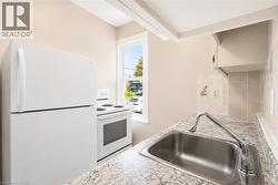 Compact kitchen featuring a stainless steel sink, a countertop with a light speckled pattern, white appliances, and a tiled backsplash - 